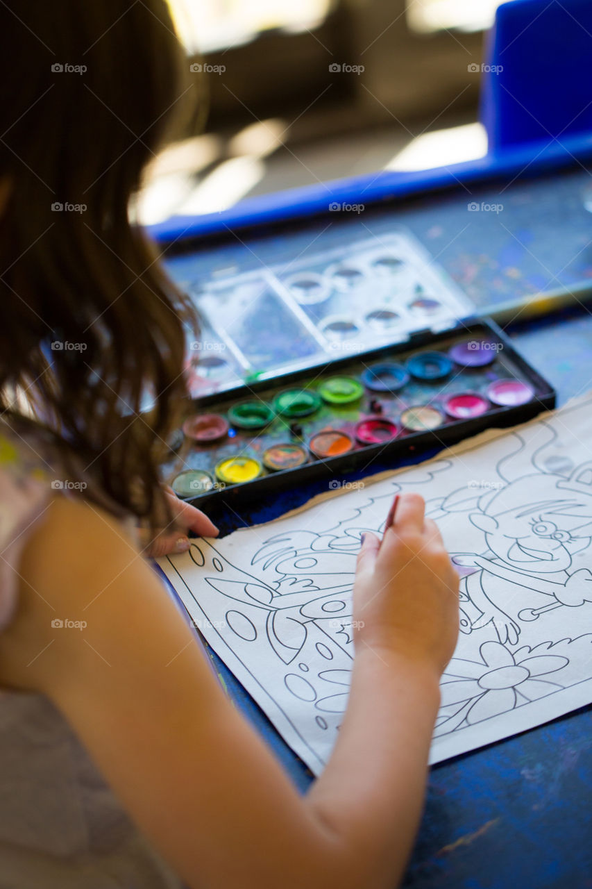 Creative at home - gpainting with water paint on blue table. Image of girl painting.