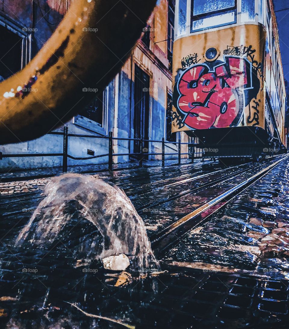 A graffitied tram ascends the hill on a rainy night in Lisbon