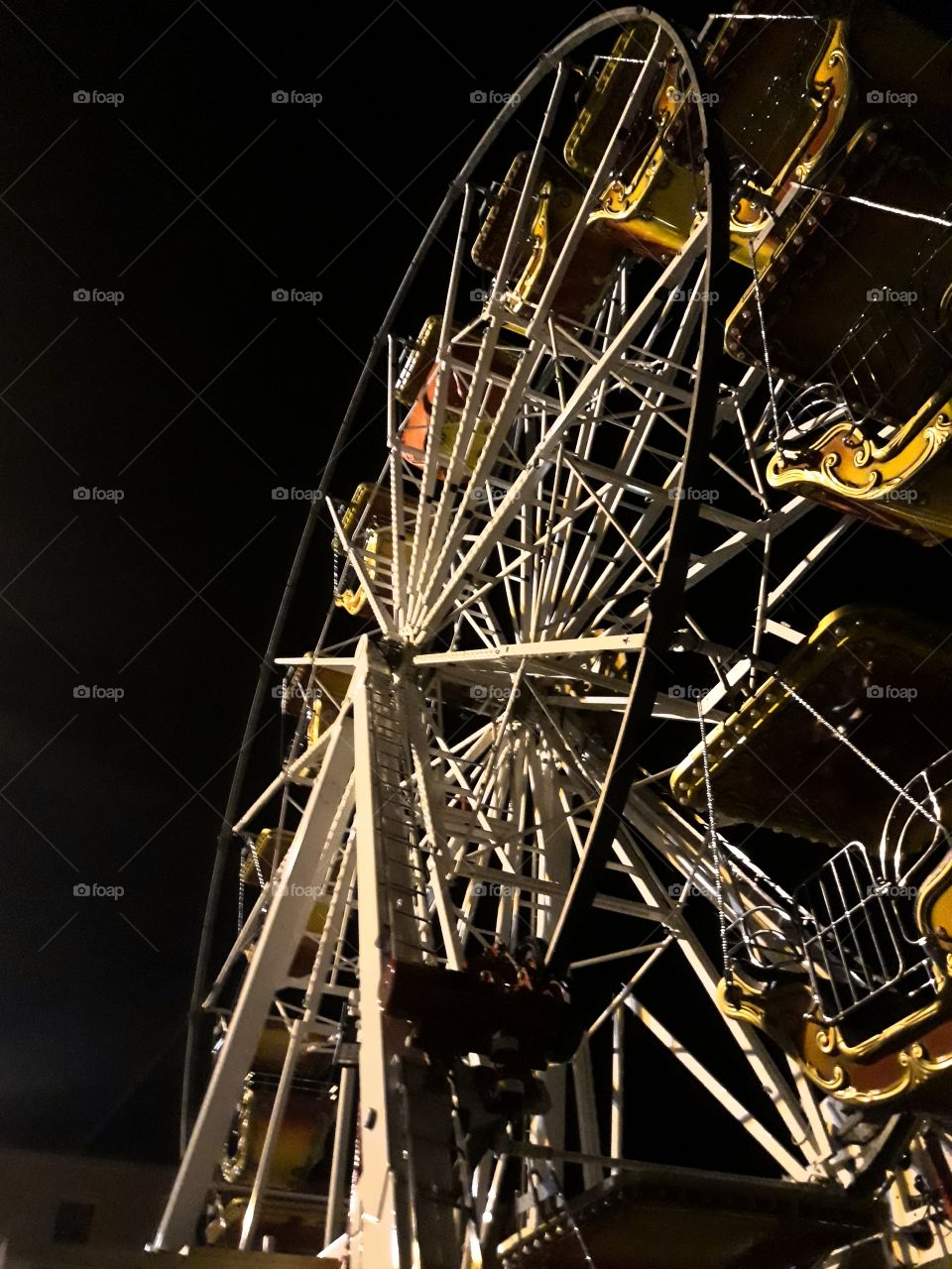 A little metal ferris  wheel photographed from below at night with a clear sky. The colours and the Shape of the Wheels recalls childhood Memories