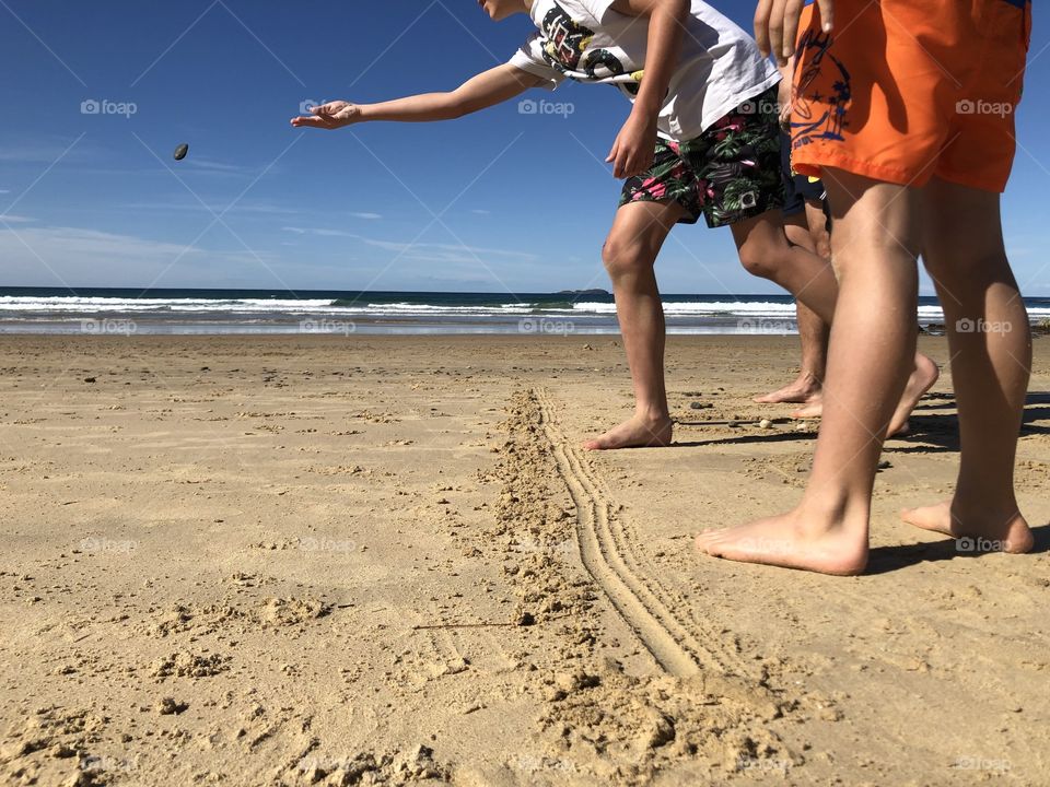 Playing a stone throwing game on the beach using a hand drawn line and stones. Bare feet children and father. 