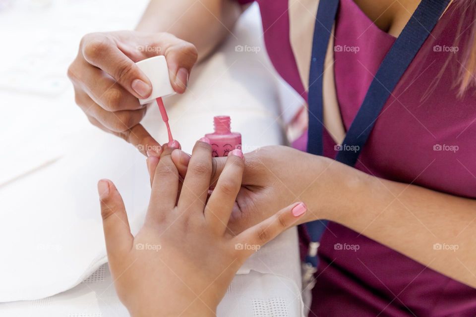 Applying pink nail polish to the nails of the child, fun at the salon