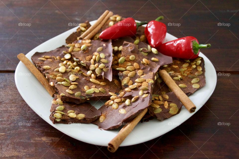 More Chocolate - Cinnamon Chocolate Chili Bark with cinnamon sticks and red chili peppers on a white plate, dark wood background 