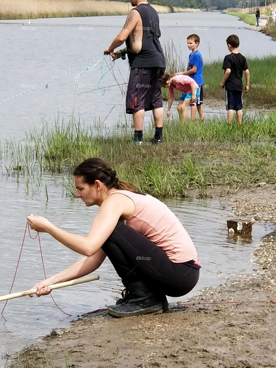 a woman in the foreground and her family in the background crabbing or fishing for crabs off of the Gulf Coast of Mexico near Bridge City Texas United States of America 2018