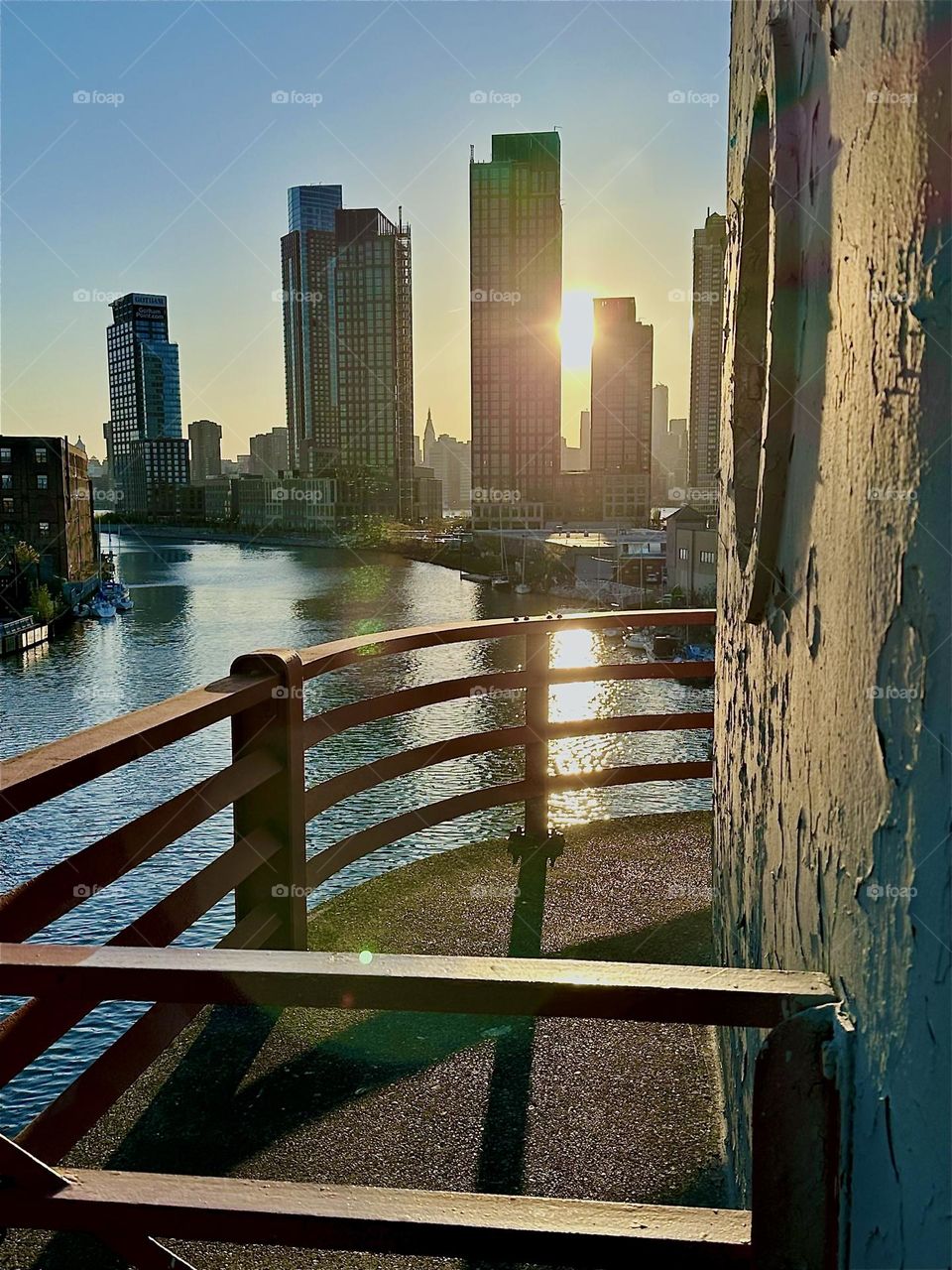 This is the central outpost of the “Pulaski Bridge” at “Newtown Creek” that connects “Greenpoint”, Bklyn to LIC, Queens in the intense light of the setting sun. Across the “East River” we see LIC and “Manhattan”. 2024. Hypnotic Productions