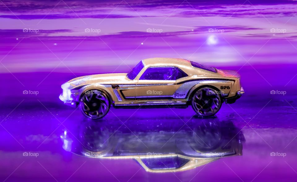 Composite image of a yellow toy car, reflected and a purple sky background that I photographed separately 
