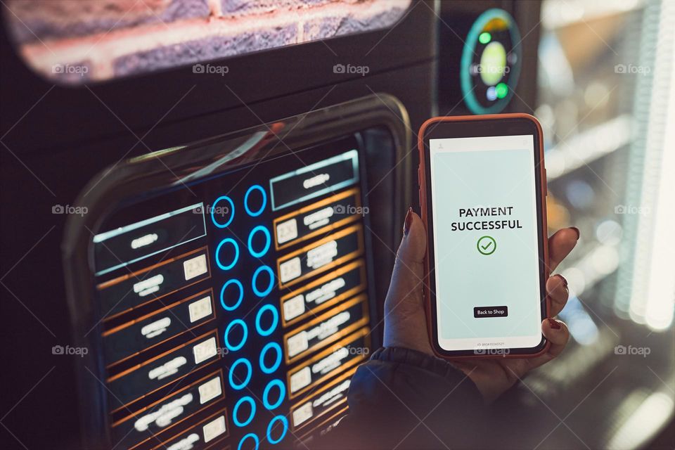 Consumer paying for product at vending machine using contactless method of payment with mobile phone. Woman using payment app on smartphone to buy product. Female hand holding smart phone with payment confirmation on screen