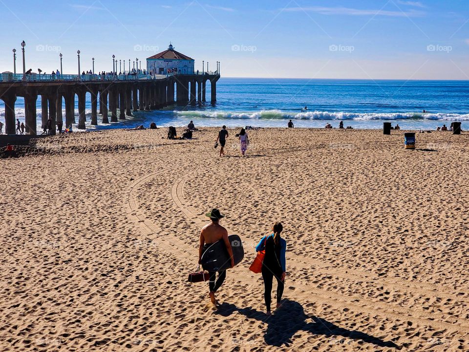 Surfers walk on a sandy beach towards the Pacific Ocean on a beautiful sunny day