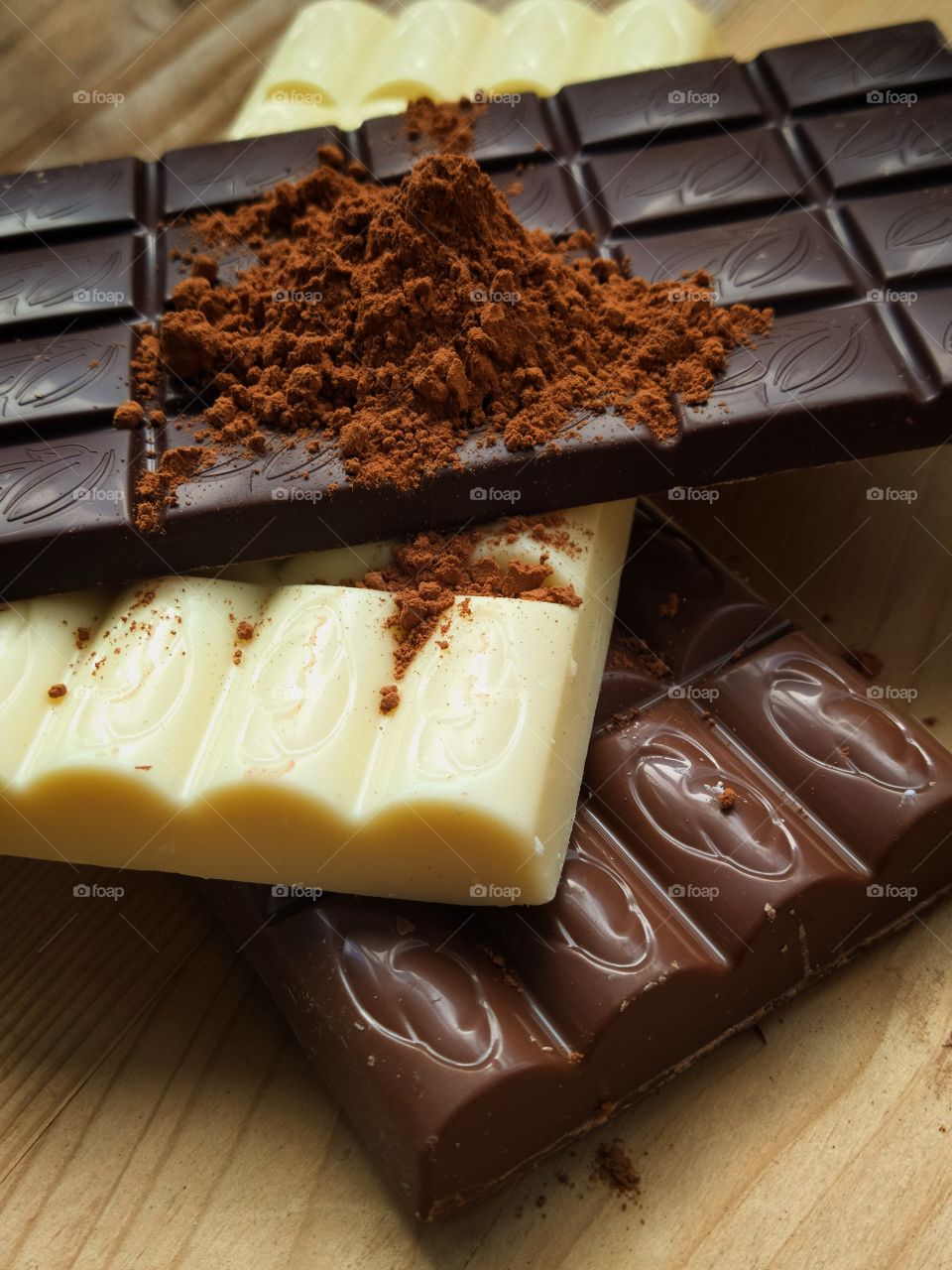 Three chocolate bars: bitter, white and milk chocolate, sprinkled with cocoa powder