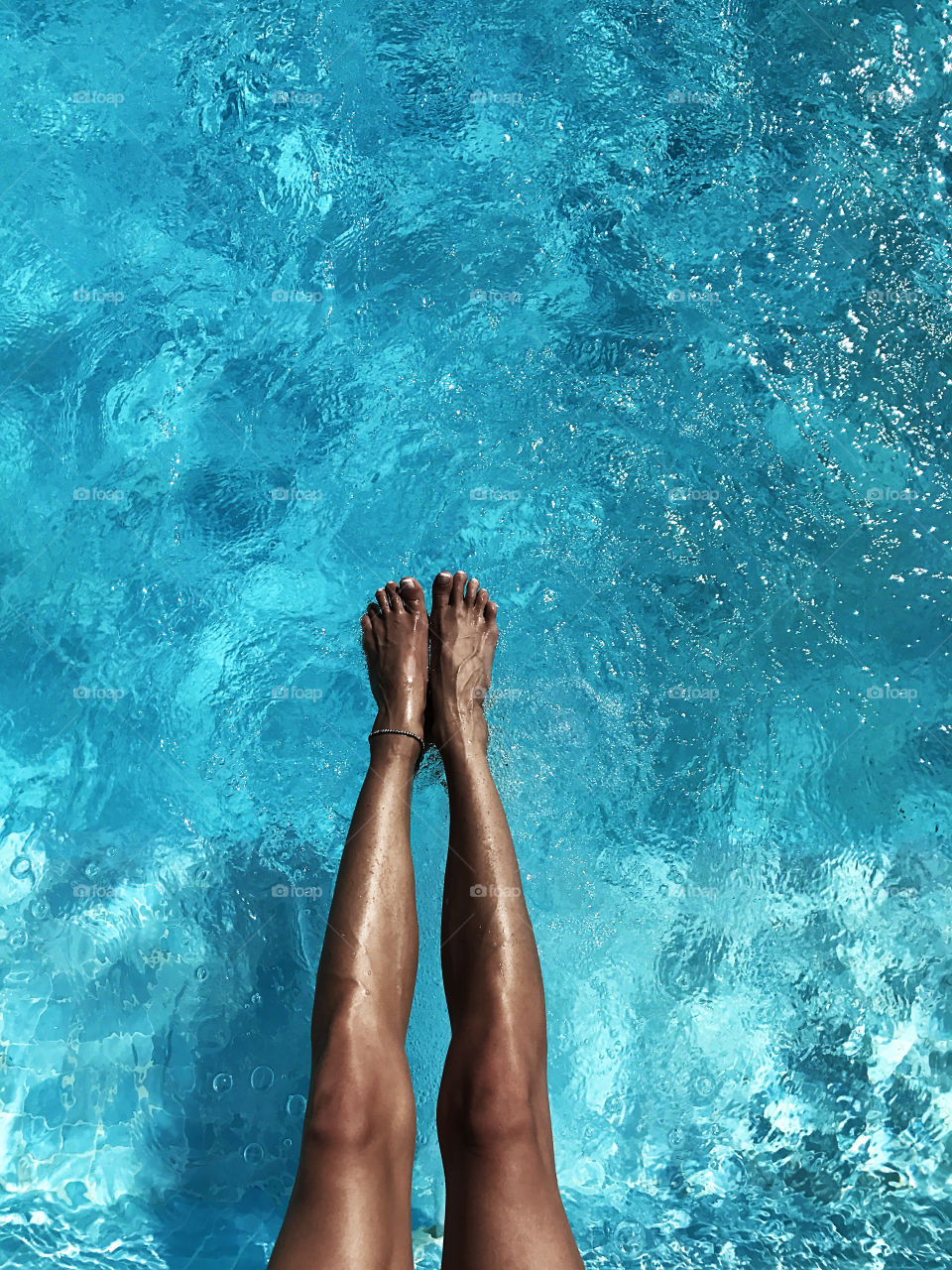 Female feet over the blue water 
