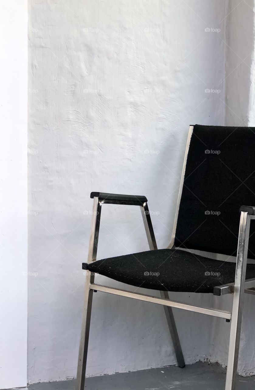 Simple metal chair with black textile against blank textured wall