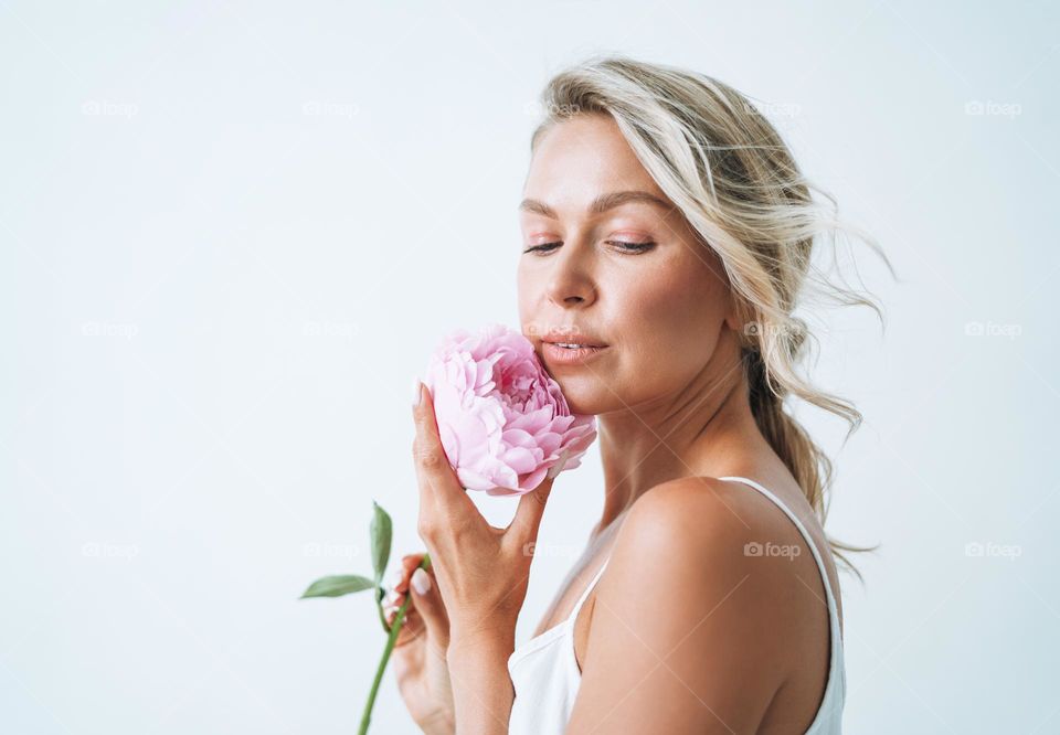 Beauty portrait of blonde hair smiling young woman with pink peony in hand isolated on white background