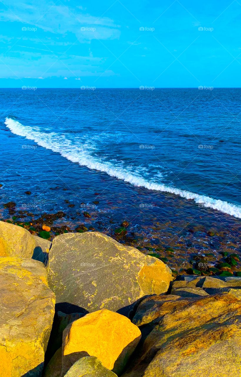 view of wave on the Atlantic ocean from a the rocky shore on a warm sunny autumn day