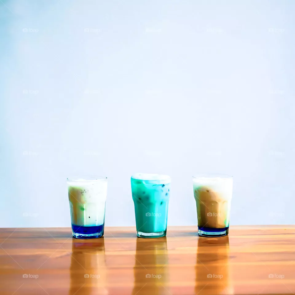 Three glasses of drink are lined up on a wooden table. Drink. Beverages. Glass. Table. Wood. Wooden table. Café. Cold. Ice. Fluid. Liquid. Photography. Aesthetic. Isolated background. Tranquil. Scene
