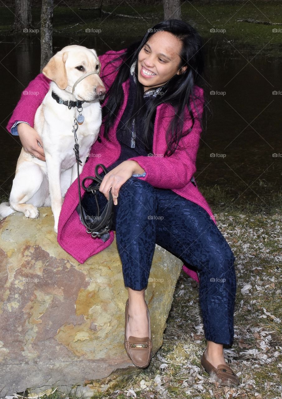 Young lady wearing a pink coat smiling at her yellow Labrador puppy