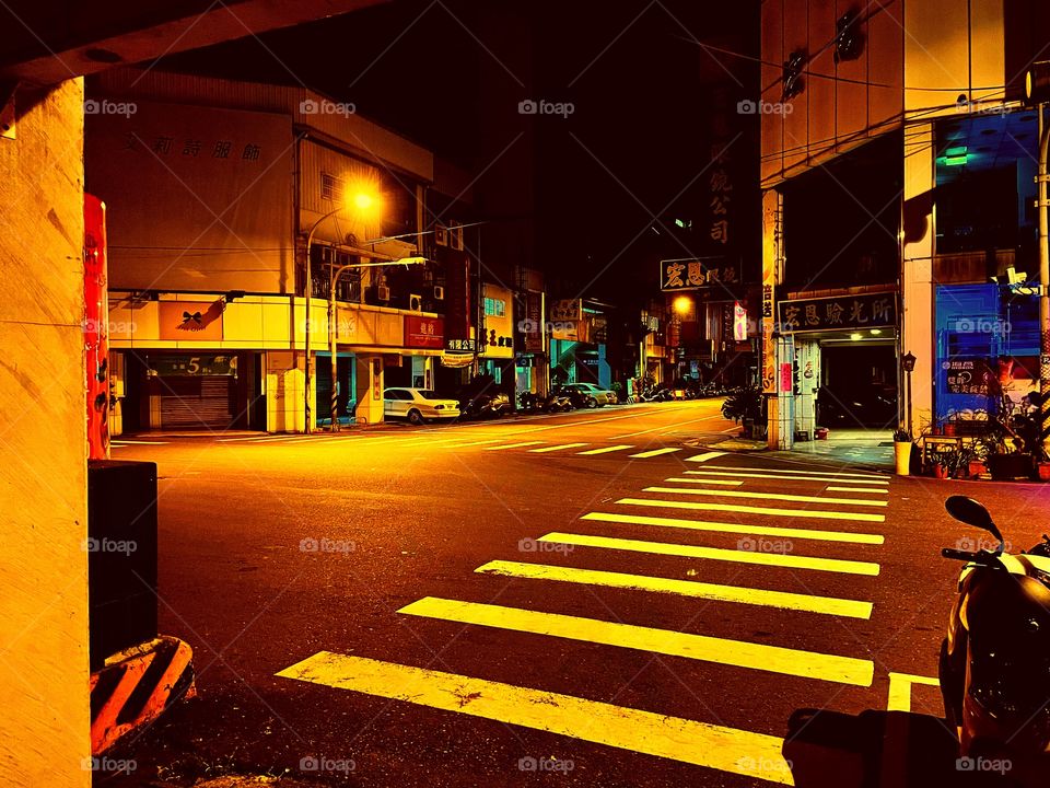 An empty intersection in Taiwan. Across the street are many businesses. It is nighttime. 