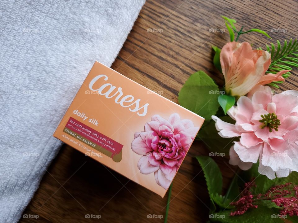 The new Caress bar single bar pack centered next to a white towel on the left,  with matching flowers on the right side, on a wood background.