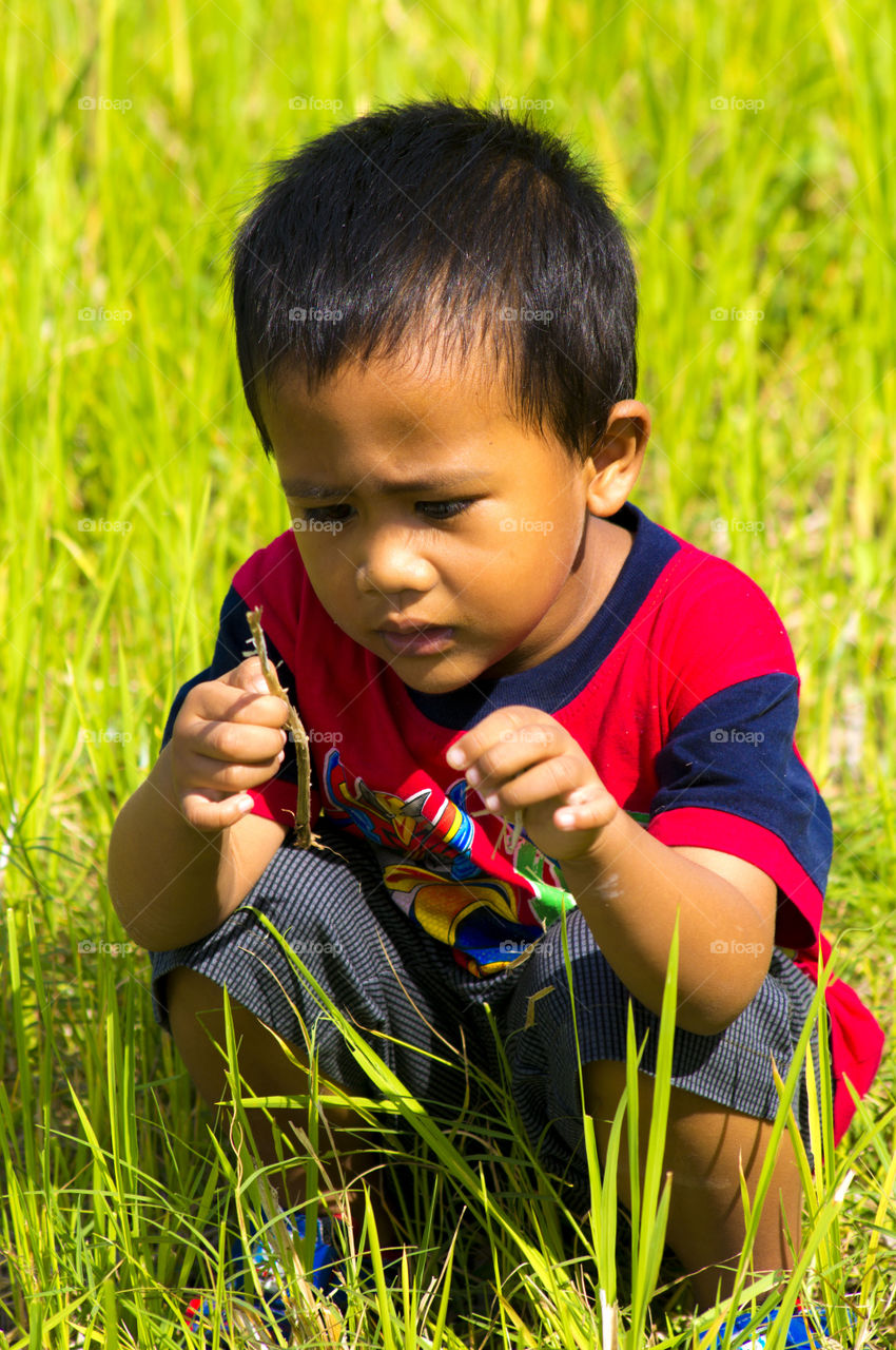 Asian boy crouching in grass looking at twig