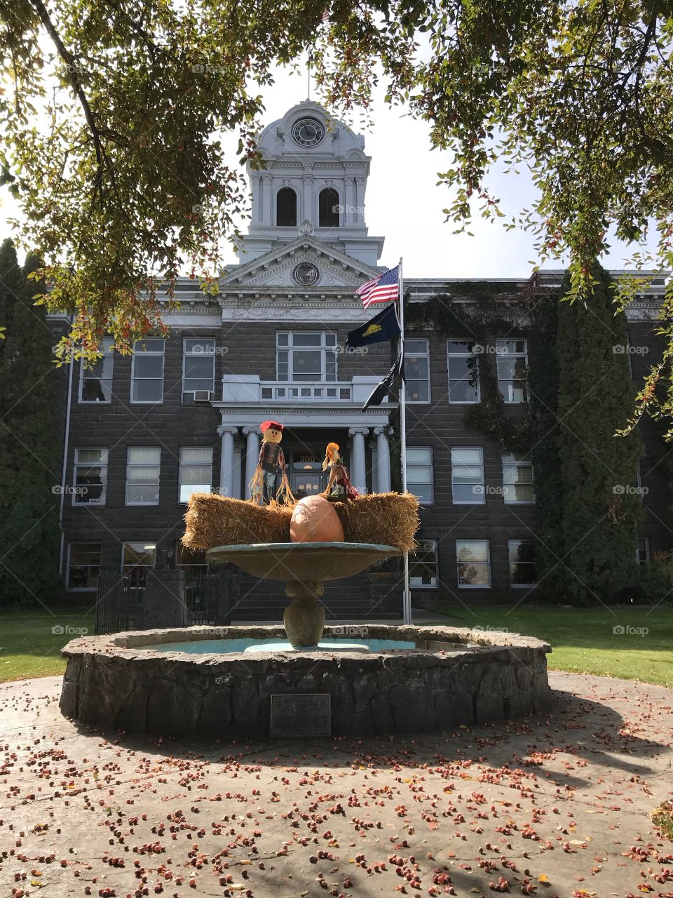 A pair of decorative scarecrows perched on hay bales with a pumpkin in the fountain at the old Crook County Courthouse in Prineville in Central Oregon on a beautiful fall day. 