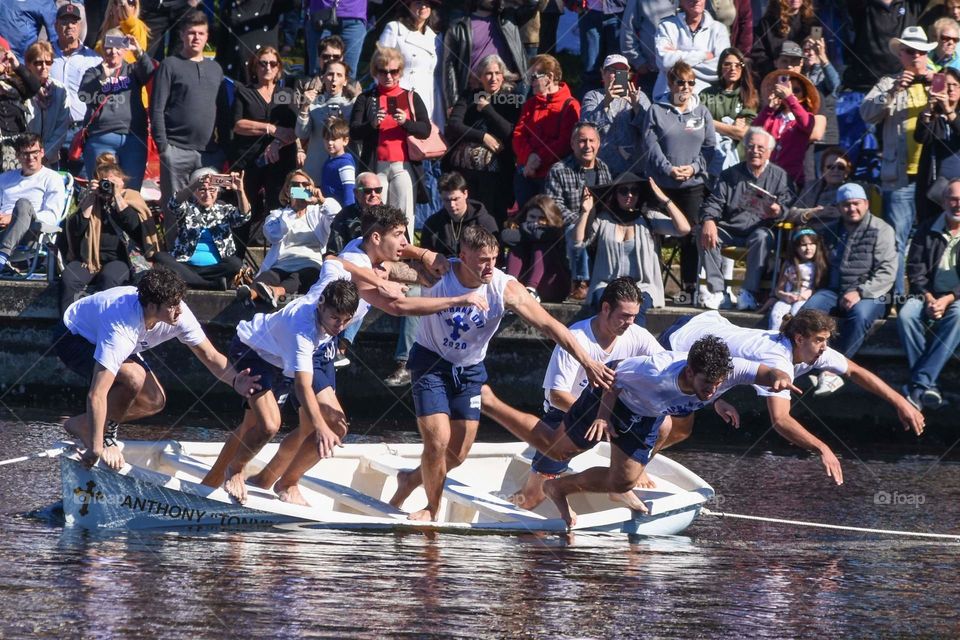 a group of boys is jumping from a boat into a bayou in a race to grab a cross during a greek religious ceremony