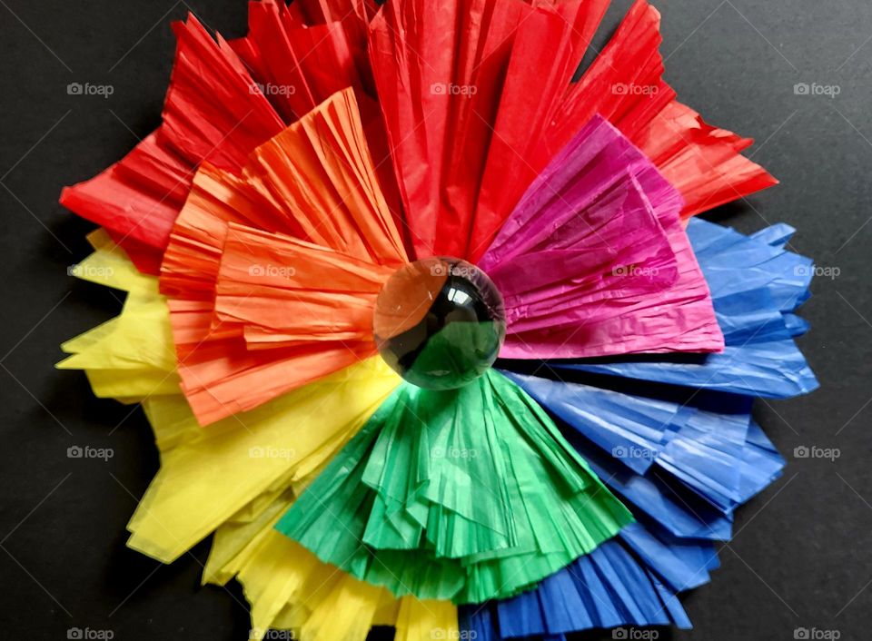 Complementary colours flatlay made out of silk papers representing a flower with a crystal ball in the centre on a black surface