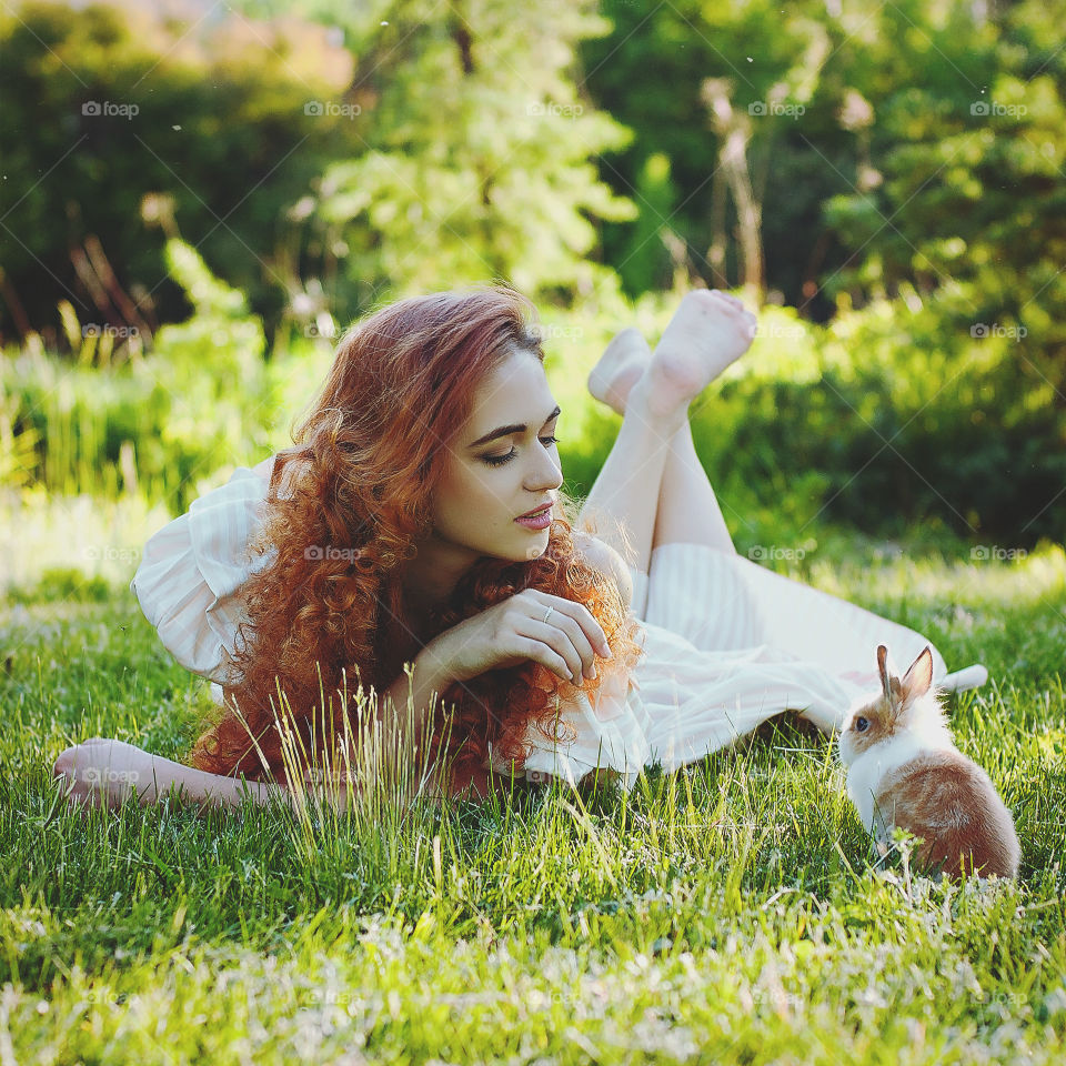 Funny redhead woman playing with rabbit in the sunny day in spring. Lifetime. Outdoor activities.