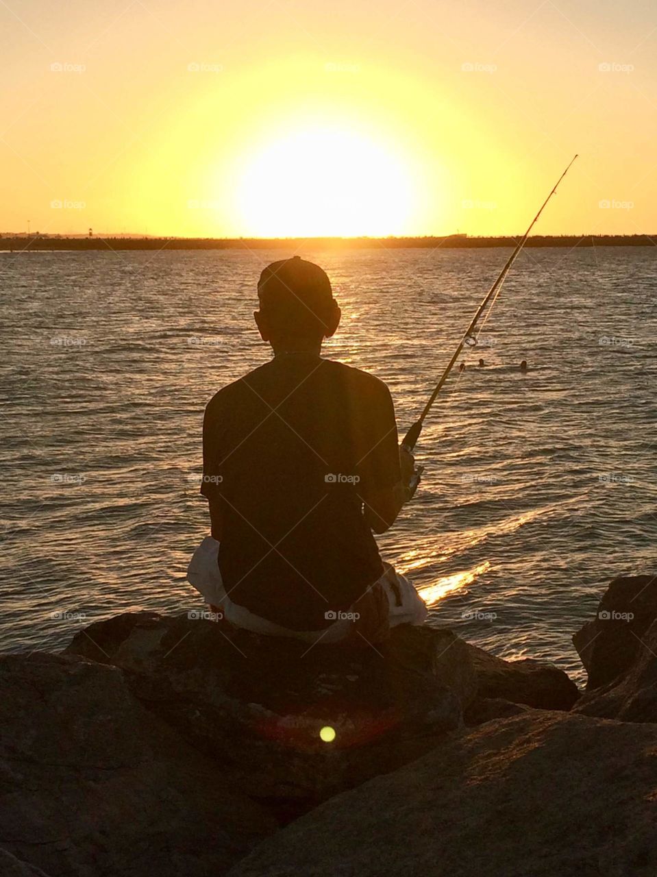 Man fishing in the sea, at sunset