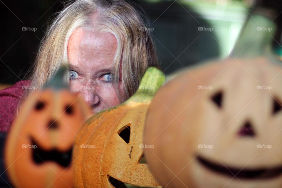 Face of a strawberry blonde woman with freckles and blue eyes between three Jack O’Lantern