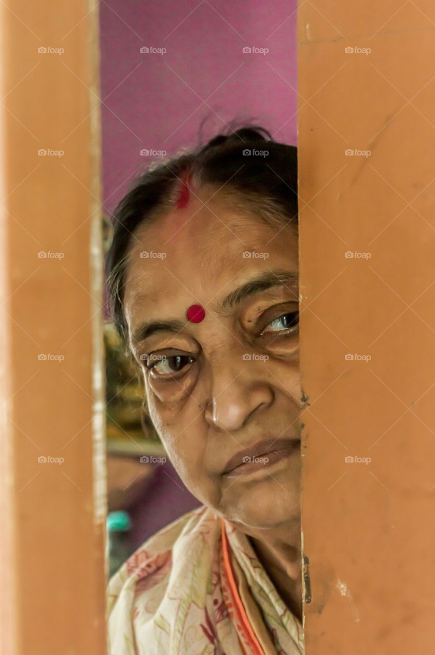 Thoughtful, sad, Worried and alone elderly senior woman peeping through the door at home and eagerly waiting for her son to come. Loneliness concept