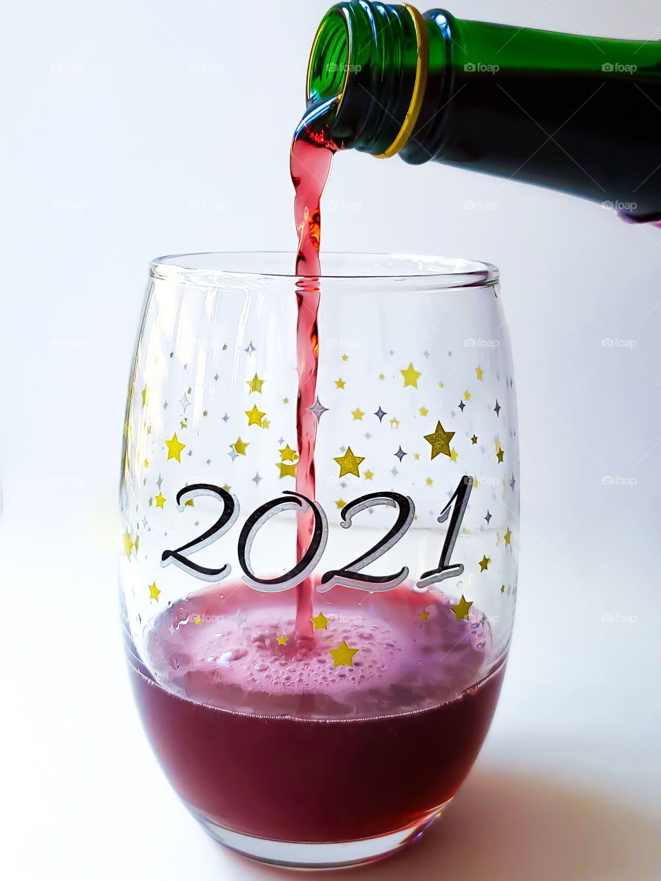 Pouring to a new year and saying goodbye to a 2020. Sparkling red wine being poured into a 2021 wine glass with a white background!.