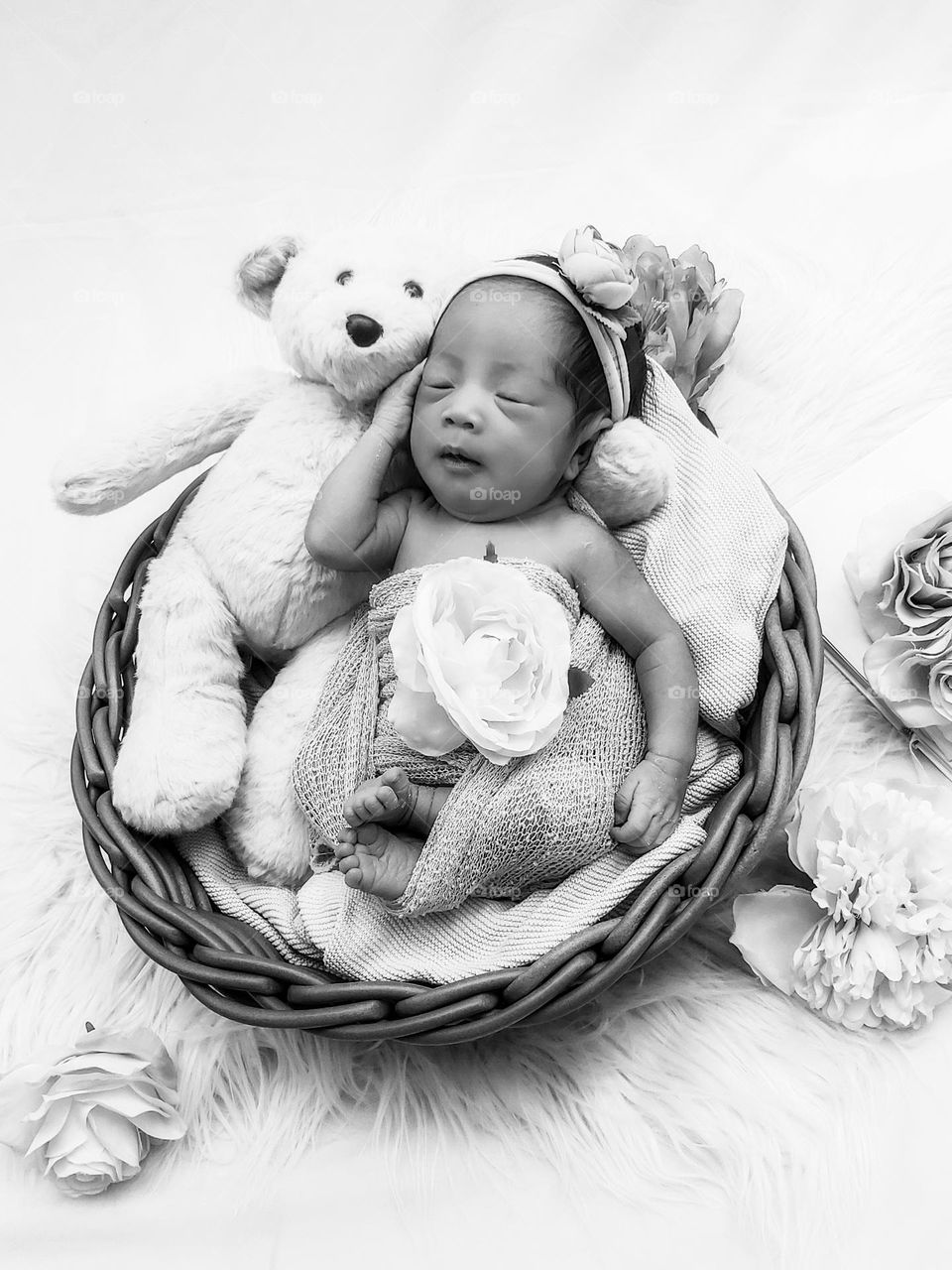 Cute baby girl sleeping with teddy bear in wicker basket bed.