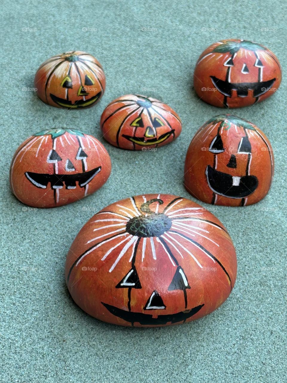 Many hand painted stone Halloween pumpkins over green sand