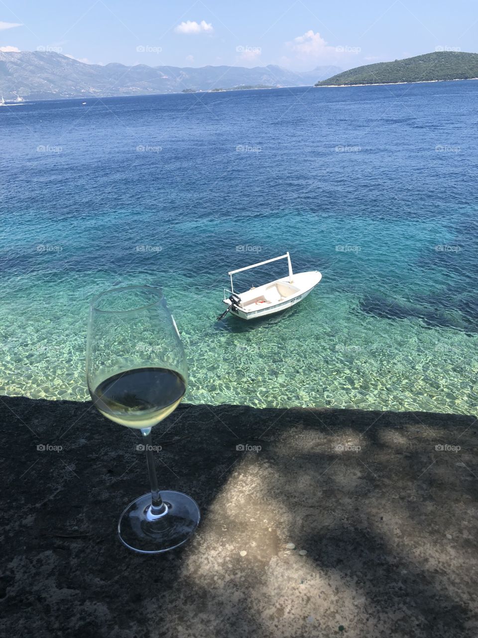 Enjoying a glass of white wine over looking the Beautiful clear green blue Adriatic Sea in Korcula Croatia Where a boat is floating in the background