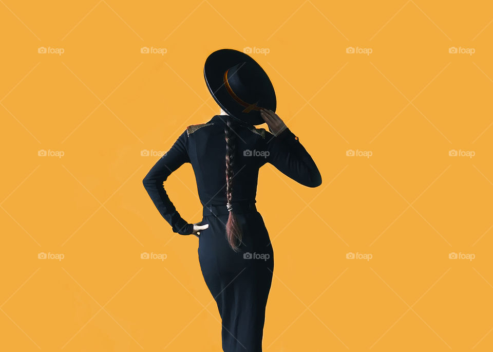 Woman in black hat and black clothes on monochrome orange background 