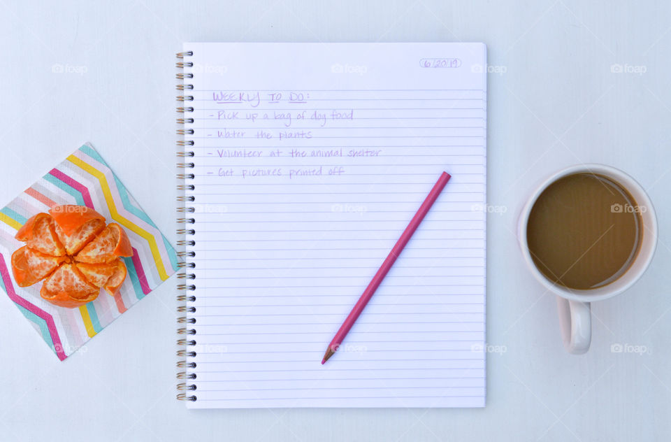 Flat lay of an open notebook with a to do list and an orange and a cup of coffee