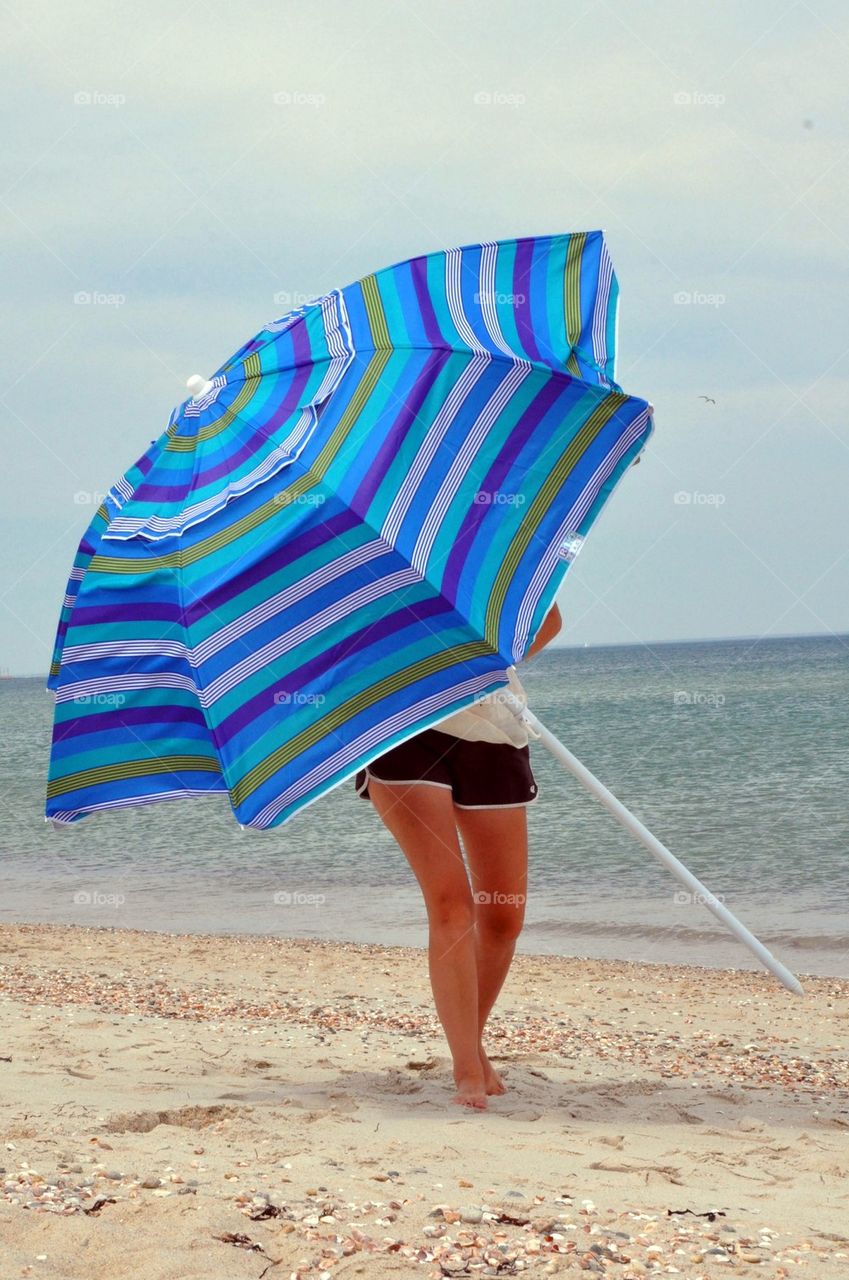 A woman is seen carrying a huge striped beach umbrella on the beach