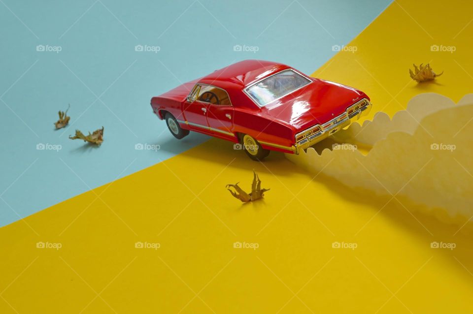 a red retro car flying at speed lets dust cut out of paper behind it. who's to say it's not a road trip