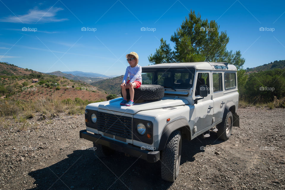 Small girl admire views of rural mountain areas in Andalucia, Spain sitting on top of a spare tyre in all terrain 4x4 car.