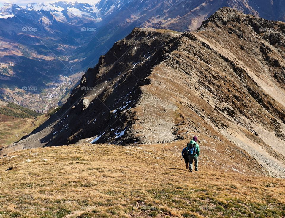Hiking down mountain with view of valley and snow mountains.