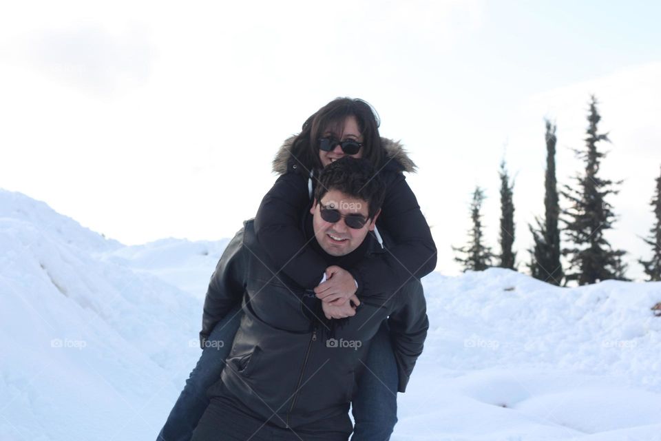Man giving wife piggyback ride in the snowy mountain