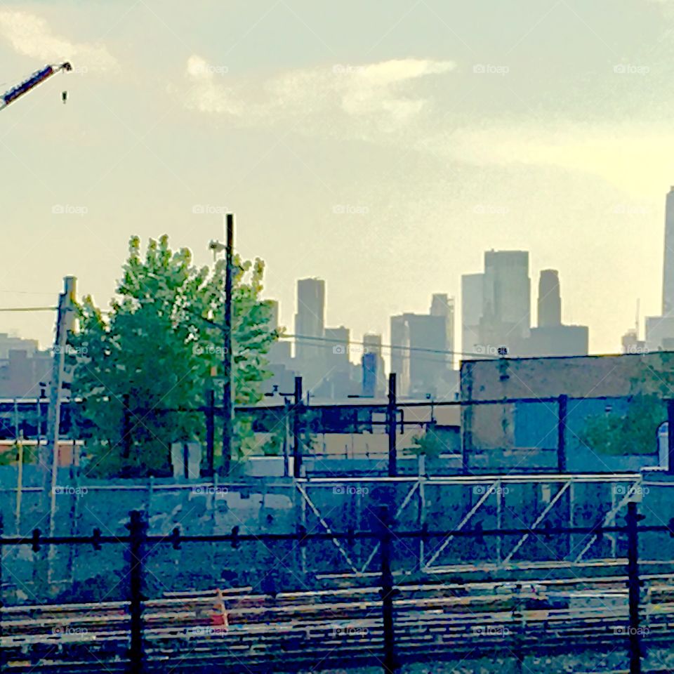A view across the train tracks by Borden Avenue in Long Island City, Queens, NY around sunset. In the distance you can see Manhattan. The sky is refracting the setting sun’s rays just faintly giving it a hint of gold. 2020. Hypnotic Productions