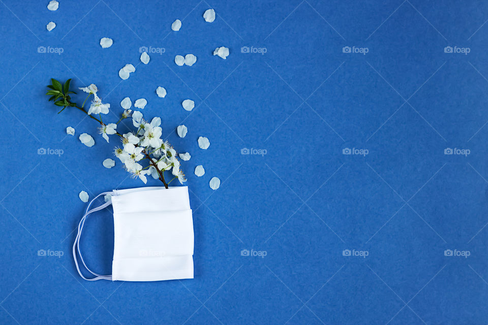 White protective mask and cherry flowers at the blue background. Concept of fight against coronavirus COVID-19. Concept of hope.