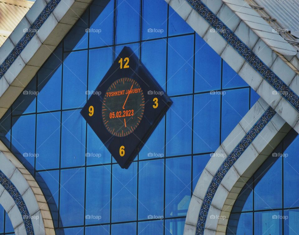 a black-framed electronic clock mounted on a mirrored building. large rectangular glasses reflect the sky. stylish station building in the capital of Uzbekistan.