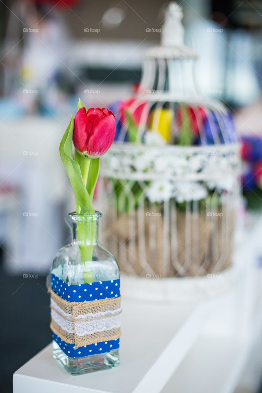 Red tulip in vase on the left of the wedding cage with flowers