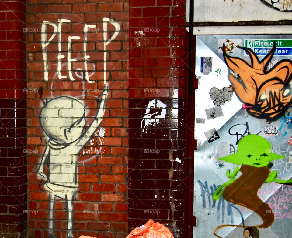 Graffiti on a wall showing various stickers and spray art. A bit writing ‘PEEEP’. 