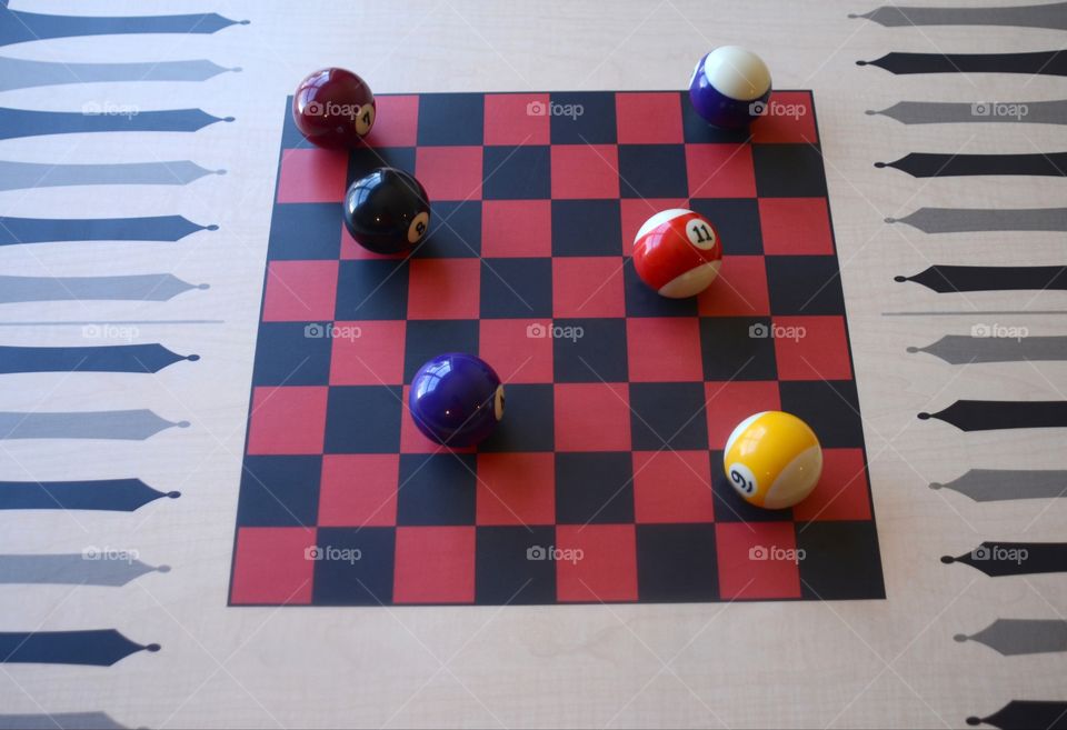 Stripe and solid cue balls sit on a black and red checker board.