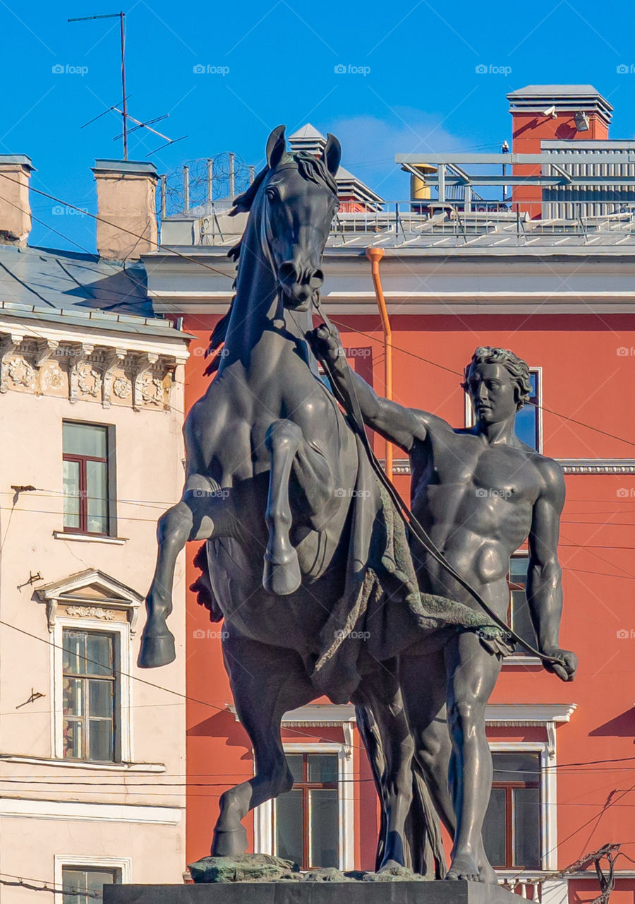 A bronze figure of a large size monument of a young man with a horse stands on a street of the city of St. Petersburg.