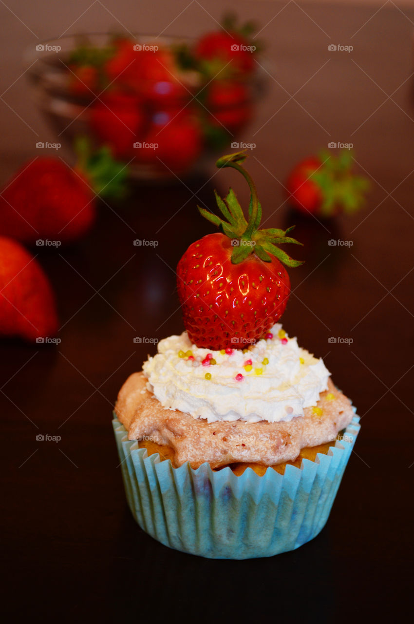 Pink cupcake with white cream and red strawberries in the background on a brown wooden table