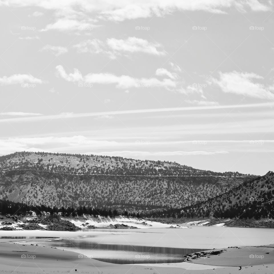 Hills covered in fresh snow and bright skies reflecting on the waters at Juniper Point at Prineville Reservoir in Central Oregon on a winter day.                                                    