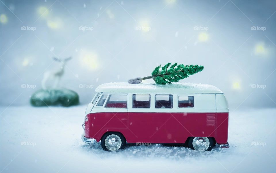Red toy camper van with Xmas tree on roof, in a snowy landscape observed by a deer