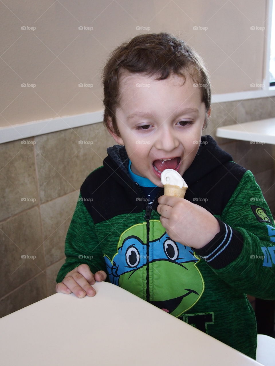 A little boy really enjoys his small vanilla cone that really hits the spot. 